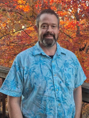man in blue shirt with leaves behind him
