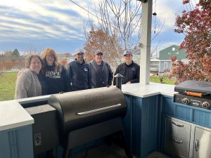 Two women and three men standing in front of an outdoor kitchen