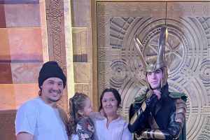 A man, woman, and child next to a Disney character
