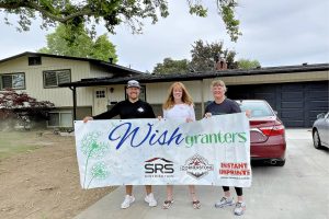 Three people holding a Wish Granters sign in front of a home.