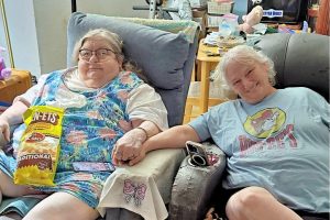 Two women sitting in recliners, holding hands